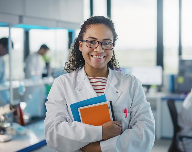 GettyImages-1346675550 A woman in lab coat holding books and smiling.