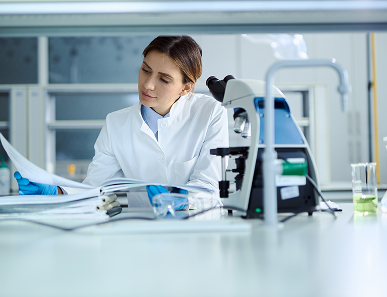 A woman in lab coat sitting at table with microscope.