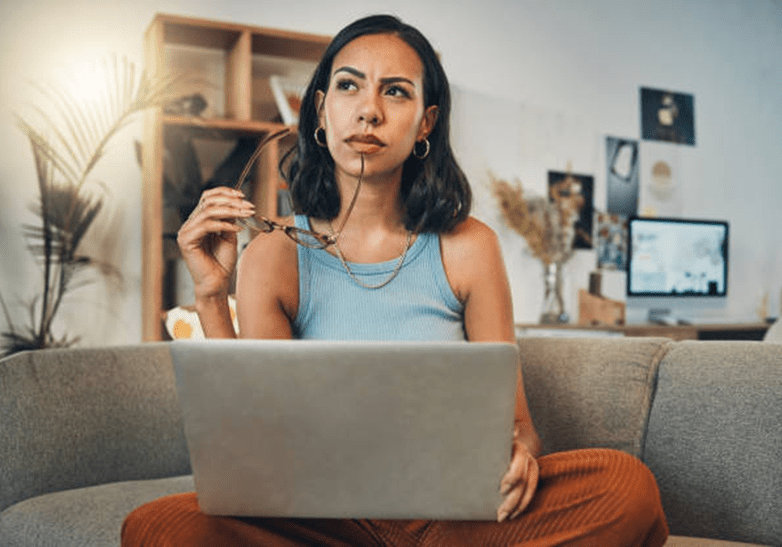 Woman thinking while holding glasses, using laptop.