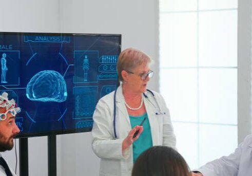 Brainwave electroencephalograph examination in hospital brainstorming office by medical physician. Monitor shows modern brain study while team of scientist adjusts the device.